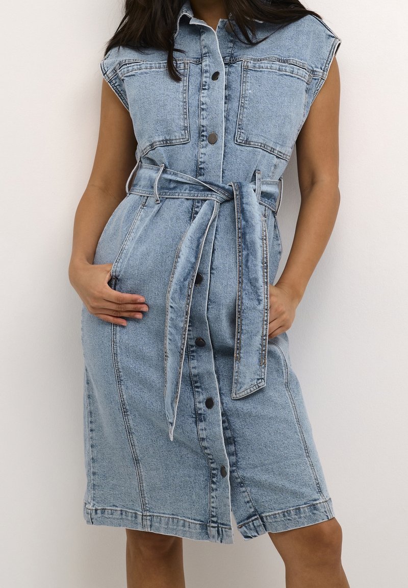 Robe en denim bleu clair avec des manches courtes, un devant à boutons et une taille ceinturée. Dispose de deux poches poitrine et de poches sur les côtés.
