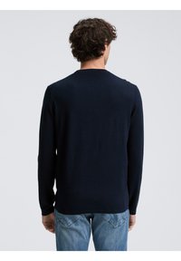 Maglione a maniche lunghe di colore navy realizzato in tessuto lavorato a maglia, con scollatura rotonda e design aderente, abbinato a jeans azzurri chiari.