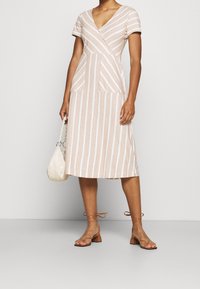 Abito midi a righe con scollo a V, maniche corte e due tasche frontali. Presenta un corpetto aderente e una gonna svasata in beige e bianco.