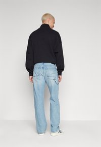 Camisa negra de manga larga con cuello alto, combinada con jeans de corte holgado de color azul claro que tienen dos bolsillos traseros y un ligero desgastado.