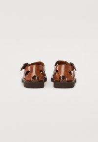 Brune lær sandaler med udskårne design, justerbar spænde lukning og tekstureret fodseng. Robust brun sål, åben bagdel for åndbarhed.
