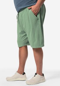 Pantaloni corti in cotone verde chiaro con cintura elastica, cordino, tasche laterali e vestibilità rilassata, abbinati a sneaker bianche.