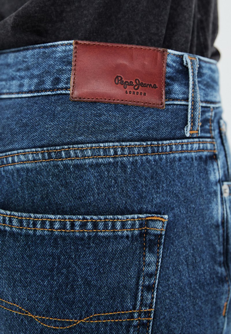 Niebieskie dżinsy mają brązową skórzaną naszywkę z napisem "Pepe Jeans London", kontrastowe szwy oraz tylne kieszenie.