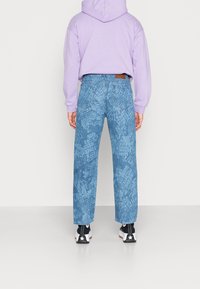 Světle fialová mikina, modré džíny se strukturovanými vzory a černé tenisky s bílými akcenty. Džíny mají vysoký pas a široké nohavice.