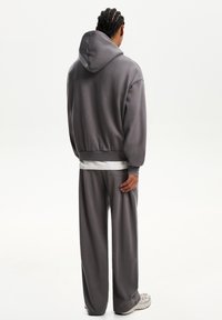 Huvtröja i grått med avslappnad passform, elastiska muddar och matchande grå vida byxor. Slät textur, minimalistisk design och inga synliga mönster.