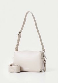 Beige crossbody bag with a smooth leather finish, rectangular shape, adjustable strap, and "Calvin Klein" logo embossed on the front.