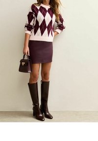 Pull bordeaux à losanges, mini-jupe en cuir ajustée et bottes marron montant jusqu'aux genoux. Sac à main structuré marron avec détail de fermoir. Textures lisses, couleurs audacieuses.