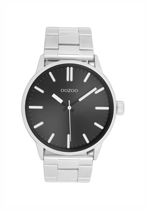 Montre-bracelet en métal argenté avec un cadran rond noir, des marqueurs des heures blancs et des aiguilles argentées. Elle possède un bracelet en acier inoxydable et une couronne proéminente.
