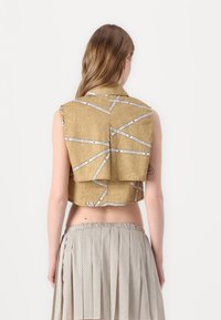 Cropped top dorato in un tessuto testurizzato, con dettagli in nastro bianco. Abbinato a una gonna plissettata a vita alta, decorata con piccoli pois.