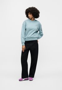 Ανοιχτό μπλε φούτερ με στρογγυλή λαιμόκοψη, σε συνδυασμό με μαύρο παντελόνι φαρδιάς γραμμής και μοβ αθλητικά παπούτσια. Λεια υφή, με ελάχιστες λεπτομέρειες.