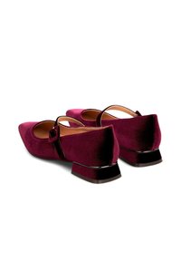 Un par de zapatos Mary Jane de terciopelo burdeos para mujer, con tacones bajos y una correa con hebilla lateral, mostrados desde la parte trasera sobre un fondo blanco.