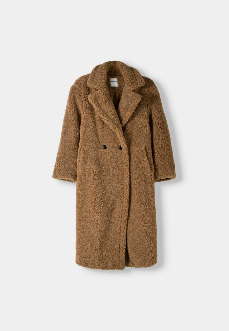 Manteau brun en matériau texturé et moelleux, avec un col châle, des boutons doublés et des poches latérales. Design mi-long.