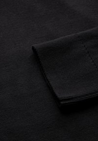 Svart stickad tröja med en slät textur, vikta ärmmuddar och en enkel design som betonar mångsidighet och en klassisk look.