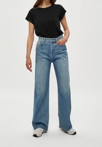 Modré džíny s širokými nohavicemi a vysokým pasem, vybavené pěti kapsami a jemně opraným lemem. Kombinovány s přiléhavým černým tričkem z bavlny.