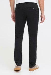 Zwarte broek gemaakt van zachte stof, met een rechte pijpdesign en twee achterzakken. Draagt met lichte schoenen.