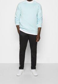 Ljusblå sweatshirt med vit kant, tillsammans med svarta joggers med vita sidränder. Vita sneakers fulländar outfiten.