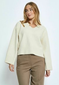 Maglione lavorato a maglia color crema con scollo a V e maniche larghe; design cropped con orlo a costine. Abbinato a pantaloni marroni sartoriali.