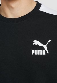 Černá mikina s kulatým výstřihem a bílými detaily na ramenou. Na hrudi se nachází bílé logo Puma. Měkká textilie.