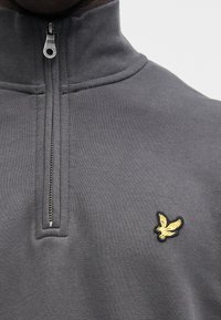 Gray zip-up sweatshirt with a high collar, made of soft fabric. Features a small yellow eagle logo on the left chest.