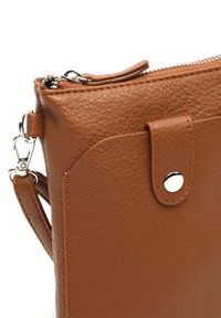 Brązowa skórzana torebka o fakturowanej powierzchni, z zamknięciem na zamek błyskawiczny i odpinanym paskiem. Posiada zapięcie na zatrzask oraz widoczne akcenty szwów.