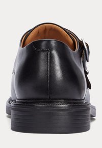 Fekete, sima bőr cipő, lekerekített formával, alacsony sarokkal és oldalsó csatos díszítéssel. A belseje barna.