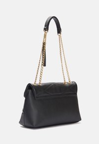 Black faux leather handbag with a quilted design, gold chain strap, and a structured shape. Features a flap closure and a tassel accent.