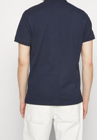 Polo bleu marine en coton, doté d'un col classique et de manches courtes. Le dos présente une texture lisse sans motifs visibles.