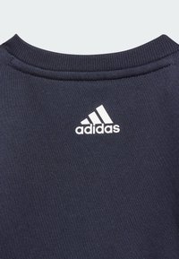 Collo del sweatshirt della marina con texture a costine. Presenta un logo Adidas bianco sopra il colletto. Design semplice e funzionale.
