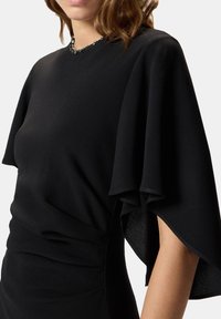 Abito nero con maniche a volant, scollo a barca decorato con dettagli di perline e silhouette aderente con dettagli arricciati.