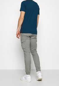 Mörkblå t-shirt med korta ärmar, i kombination med grå cargobyxor med elastiska muddar och sidofickor, bärs med vita sneakers.