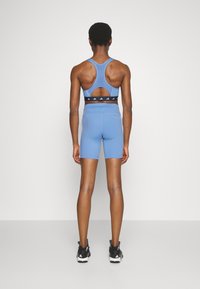 Soutien-gorge de sport bleu avec un design dos nageur et un détail découpé, associé à un short taille haute assorti. Marquage texturé noir sur la ceinture.