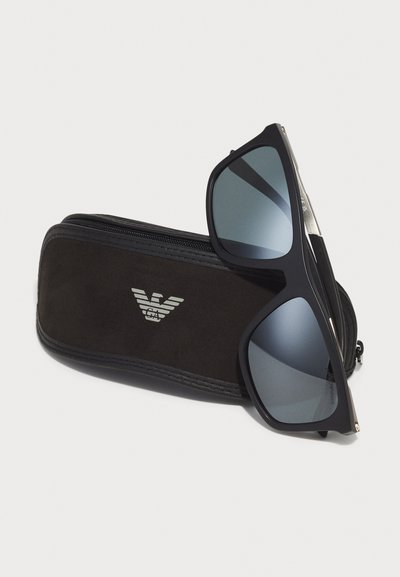 Ochelari de soare negri cu lentile mirror, având o ramă elegantă. Însoțiți de un toc negru cu fermoar, cu un logo argintiu pe față.