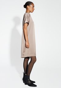 Beiges Satin-Kleid mit kurzen Ärmeln und gerader Silhouette, kombiniert mit schwarzen Ankle Boots mit niedrigem Absatz und strukturiertem Finish.