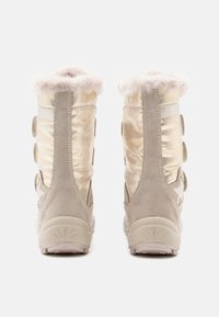 Botas em suede bege claro e tecido dourado brilhante com acabamento de pelúcia falsa na parte superior, apresentando três tiras circulares de Velcro nas laterais.