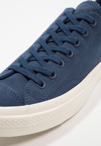 Baskets bleu marine avec dessus en daim, bout rond et semelle en caoutchouc plate. Dotées de lacets foncés et de coutures, ainsi que d'œillets ronds.