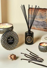 Voluspa-ljus med svarta mönstrade behållare, en svart diffusor med pinnar, och vaniljbönor på en krämfärgad yta, kork från mousserande vin ingår.