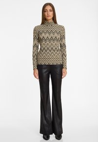 Beige Turtleneck-Top mit schwarzen Zickzacklinien, kombiniert mit eng anliegenden schwarzen Lederhosen mit Schlag. Glatte Textur im gesamten Design.