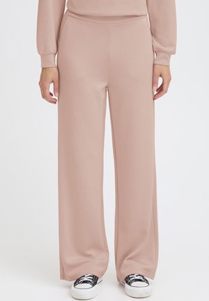 Hellrosa Hosen mit weitem Bein aus einem weichen Stoff. Sie zeichnen sich durch eine glatte Textur und einen elastischen Bund aus und werden mit schwarzen Sneakers kombiniert.
