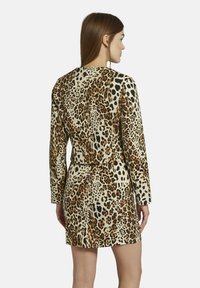 Leopardprint jurk met lange mouwen, beige basis en textuurstof. Beschikt over een getailleerd silhouet en een achteropening voor bewegingsvrijheid.