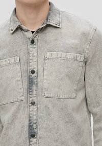 Overhemd in vervaagd grijs denim met twee borstzakken, contrasterende stiksels en een klassieke kraag. Glad, textuurachtig materiaal.
