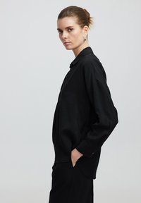 Camicia nera con bottoni, dal taglio morbido, in tessuto testurizzato, maniche lunghe e orlo curvo, abbinata a pantaloni neri.