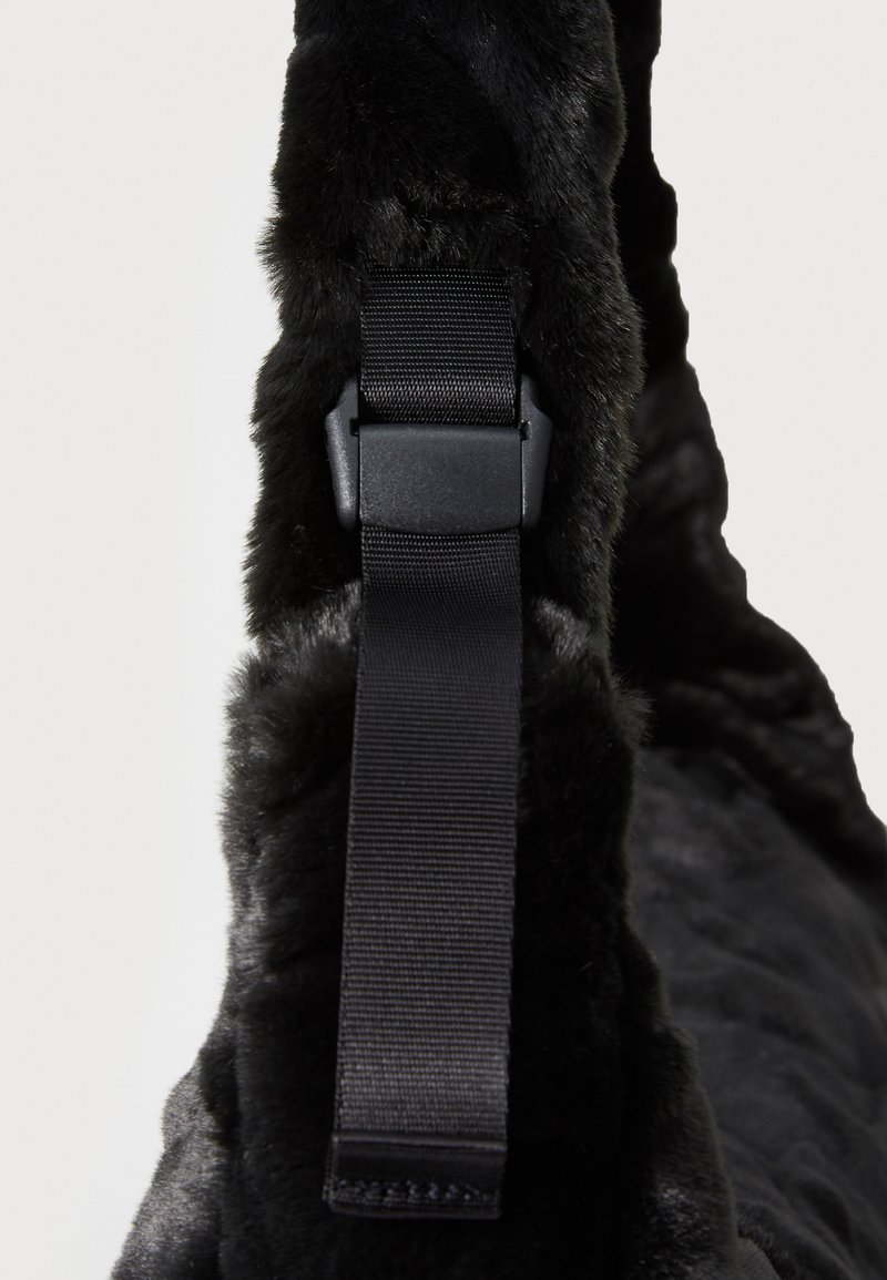 Il prodotto in pelliccia sintetica nera presenta una superficie texture, una tracolla nera regolabile e un design elegante con bordi arrotondati.