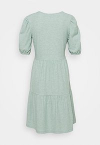 Vihreä kuvioitu mekko, jossa on lyhyet puffihihat, pyöreä pääntie ja kerroksellinen hameen muotoilu. Pehmeä materiaali.