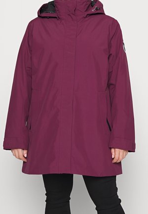 Długa, śliwkowa kurtka z kapturem z przednimi kieszeniami, czarną podszewką, noszona na czarnych spodniach, ręce swobodnie opuszczone wzdłuż ciała.