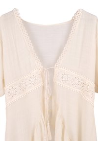 Blusa beige chiaro con scollo a V, bordino in pizzo e un nastrino decorativo sul davanti. Tessuto fluido con una consistenza leggera e maniche corte.