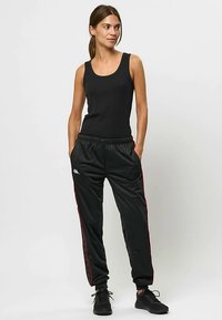 Sort tank top med rund halsudskæring kombineret med sorte træningsbukser med røde sidelister og elastik i taljen. Sorte sneakers fuldender looket.