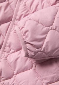 Vaaleanpunainen tikattu puffatakkikangas, jossa on pehmeä rakenne, kaarenmuotoiset ompelukuviot ja tiukka hihansuu.