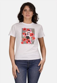 T-shirt bianca in cotone con una stampa grafica di una donna in nero con occhiali da sole, circondata da fiori rossi e rosa su strisce in bianco e nero.