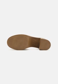 Sole di scarpa con tacco alto color beige, dalla texture liscia, di forma ovale e con un design di grip a motivi. Presenta un tacco leggermente sollevato e bordi arrotondati.