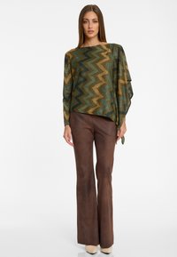 Haut à motifs zigzag vert et or avec des manches drapées, associé à un pantalon évasé marron. Texture lisse avec un léger éclat.